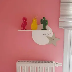 Ayyıldız rafın pembe duvarda yakın görünümü; gözleri kapalı ay ve yıldız figürleri, üstünde renkli süs objeleri
