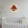 Çilekli gezegen ahşap gece lambası, bulut süslemeli bebek odasında beyaz beşiğin üstünde sıcak ışığı açık halde
