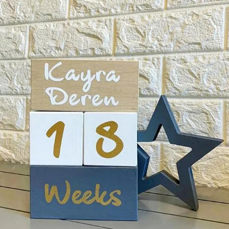 Gri mavi renkteki içi boş yıldız, isim yazılı, 18 ve Weeks yazan üst üste dizili anı küplerinin yanında