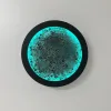 Dolunay RGB duvar lambası, siyah gövdesi ve turkuaz ışığı açık haliyle beyaz duvarda önden görünüm