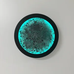 Dolunay RGB duvar lambası, siyah gövdesi ve turkuaz ışığı açık haliyle beyaz duvarda önden görünüm