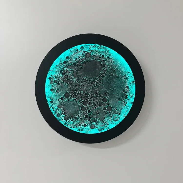 Dolunay RGB duvar lambası, siyah gövdesi ve turkuaz ışığı açık haliyle beyaz duvarda önden görünüm