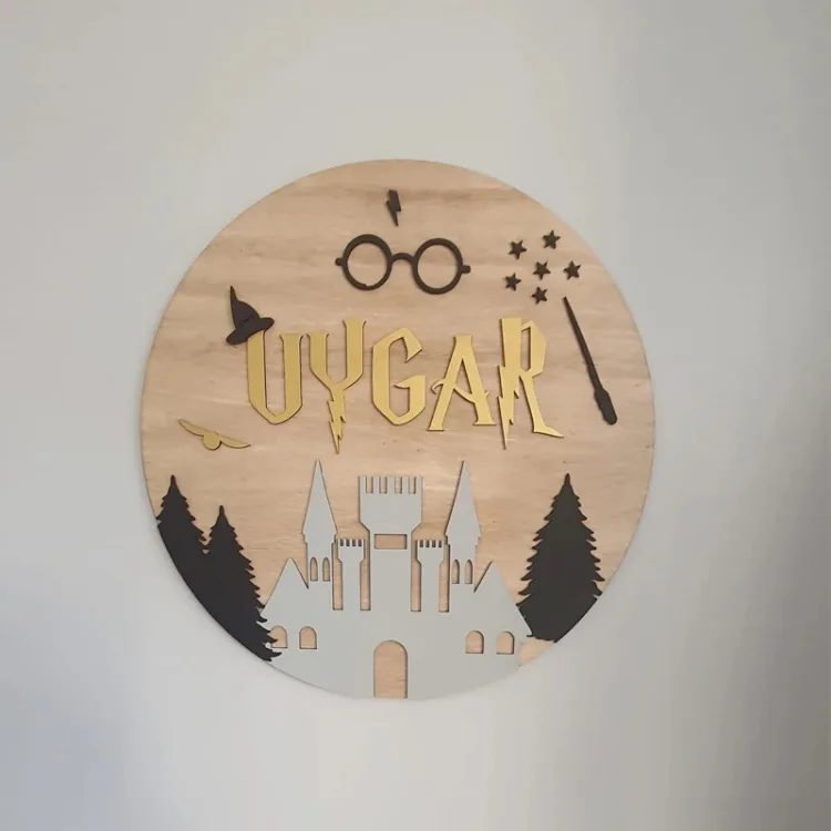 Harry Potter temalı kapı süsü duvarda önden; ahşap zeminde gözlük, şimşek, asa, kanatlı top ve altın harfli örnek isim