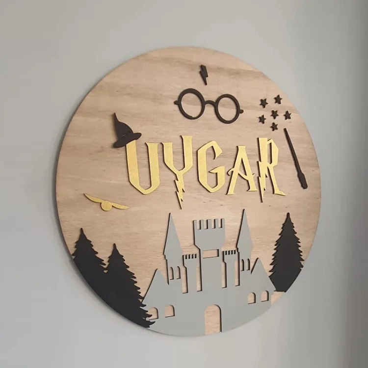 Harry Potter kapı süsünün yandan yakın planı; altın sarısı örnek isim, büyücü şapkası, yıldızlar, gri şato ve çam ağaçları