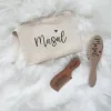İsme özel ahşap bebek saç fırçası, örnek isim baskılı çanta ve tarakla birlikte beyaz peluş üstünde, yukarıdan