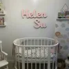 İsme özel ışıklı ahşap lamba, pembe renkte çift isim yazılı halde bebek odasında beşiğin üzerinde