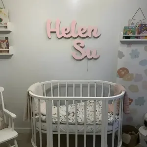 İsme özel ışıklı ahşap lamba, pembe renkte çift isim yazılı halde bebek odasında beşiğin üzerinde