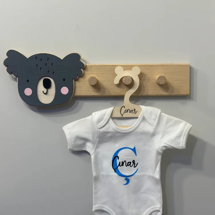 Koala figürlü askı önden; pembe yanaklı antrasit koala başı, isim yazılı elbise askısında beyaz bebek kıyafeti