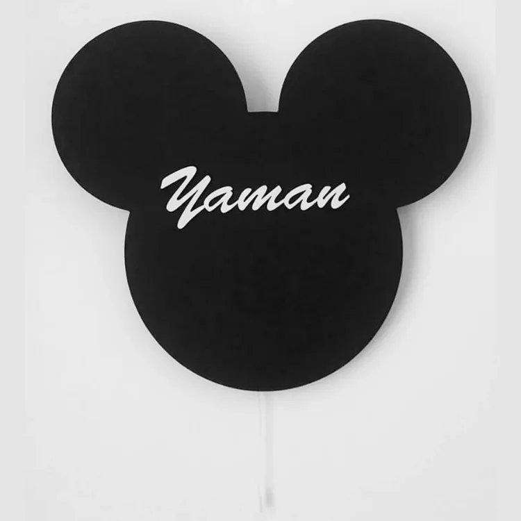 Mickey lambanın siyah modeli ışığı kapalı halde beyaz duvarda; ortada beyaz el yazısıyla örnek isim ve çekme ipi