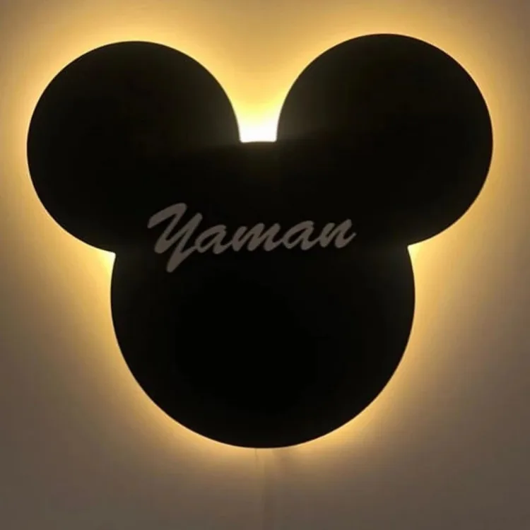 Mickey lambanın yakın planı; siyah kulaklı formun arkasından yayılan sıcak sarı ışık ve açık renk örnek isim yazısı