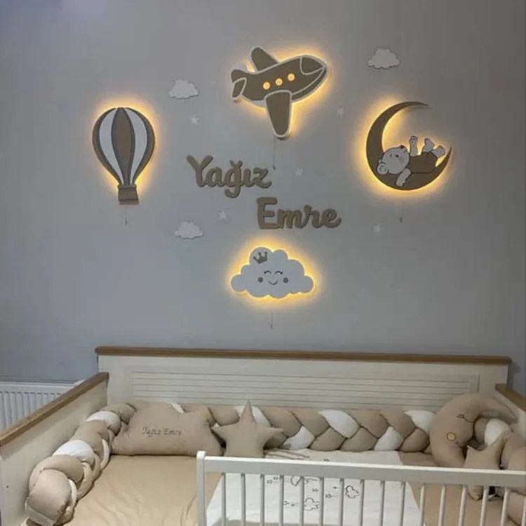 Uçan balon, uçak, bebek ayılı ay ve gülen bulut lamba, ortada ışıksız ahşap isim, gri duvarlı bebek odasında