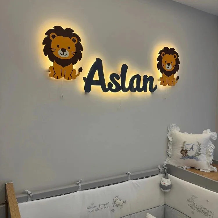 İki yanında aslan lambaları olan ışıklı isim lamba, bebek odasının gri duvarında yakından