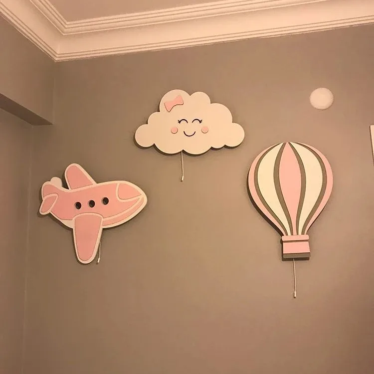 Pembe uçak, gülen yüzlü bulut ve pembe çizgili uçan balon ahşap lamba, bej duvarda yakından