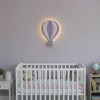 Uçan balon ahşap gece lambası, lila duvarda beyaz bebek karyolasının üzerinde ışığı açık, mor ve pembe dilimli